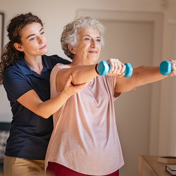 woman assists an older woman as she lifts dumbbells during a workout session.