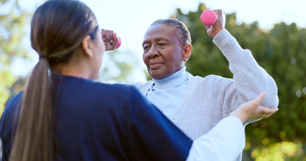 Senior woman working out with dumbbells and a trainer as part of the benefits of independent living facilities 